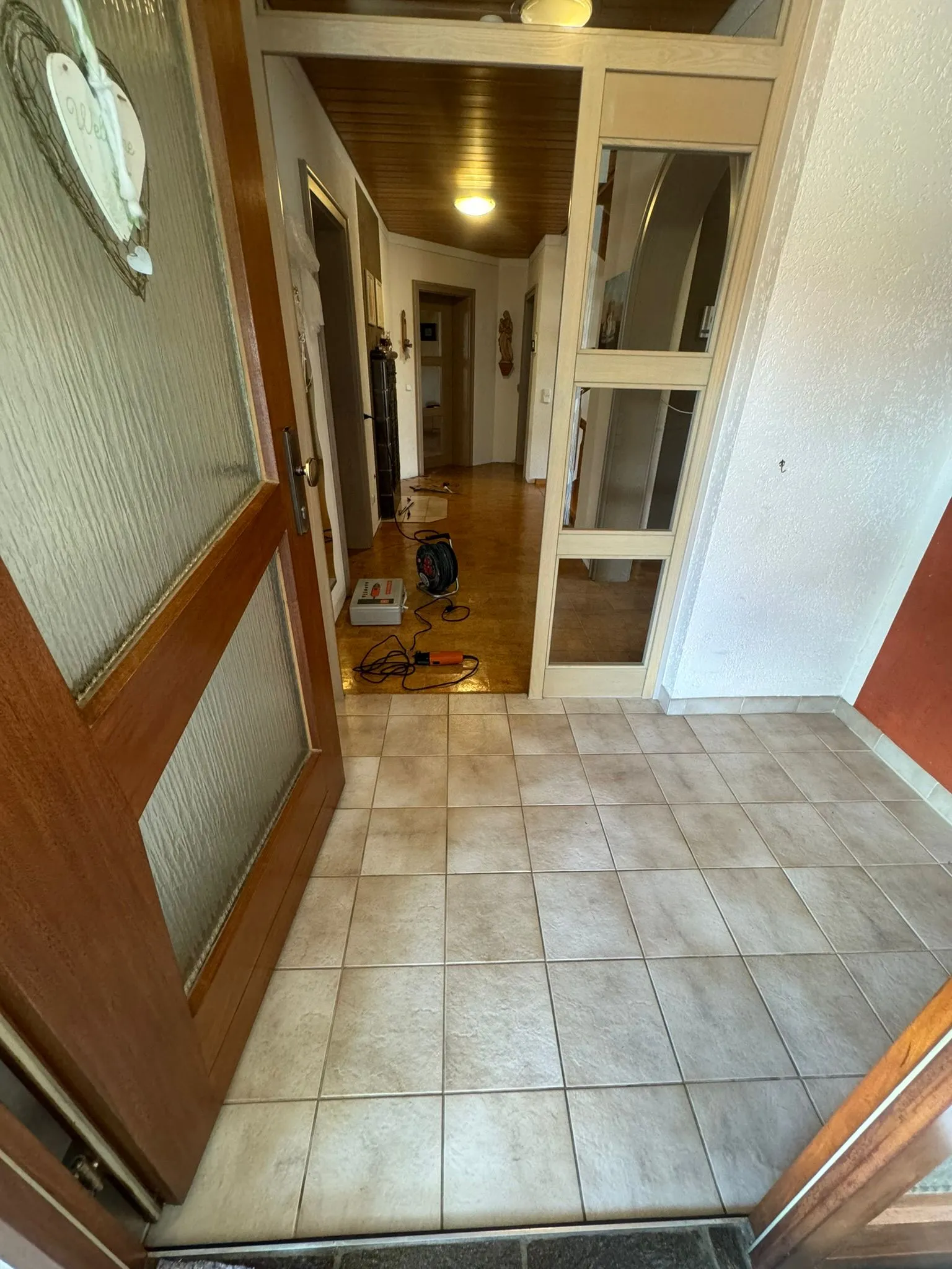 Derselbe Flur vorher: alte beige Fliesen mit Werkzeug und Kabeltrommel