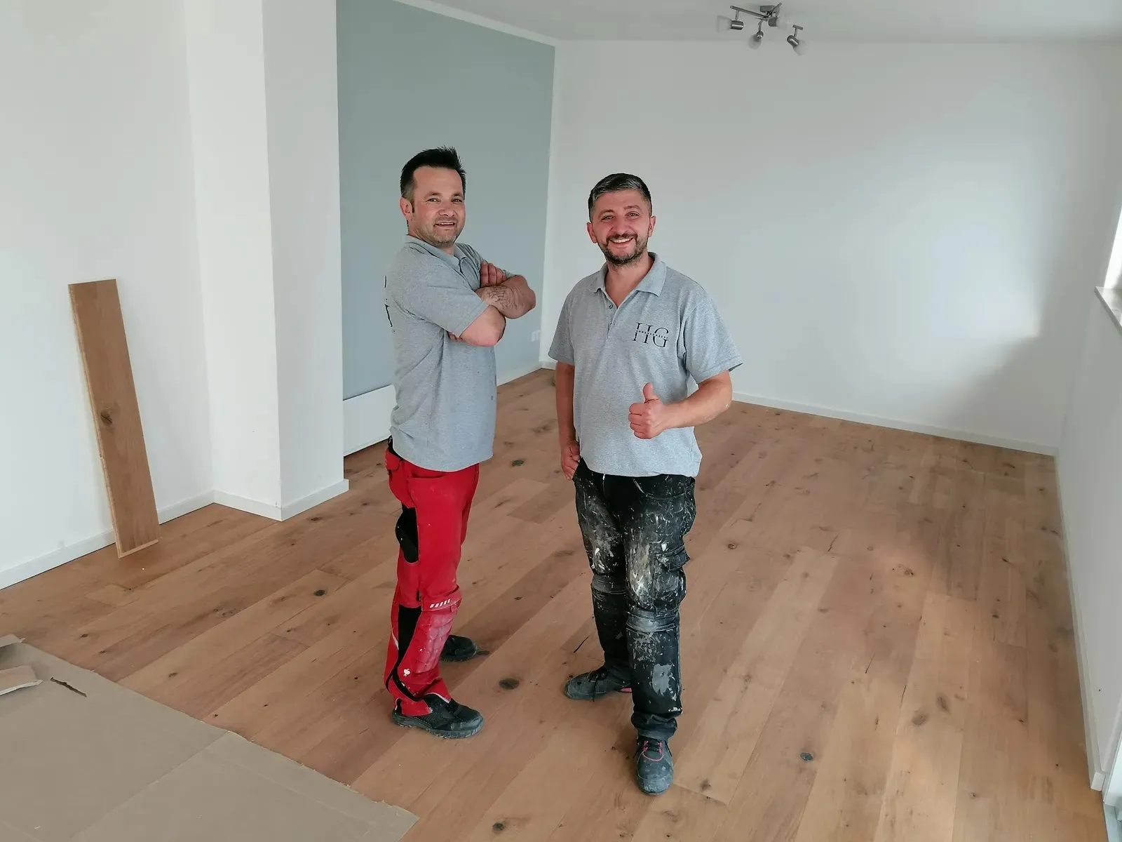 Zwei Handwerker von HG Bodenkonzept mit Daumen hoch auf frisch verlegtem Eichenparkett