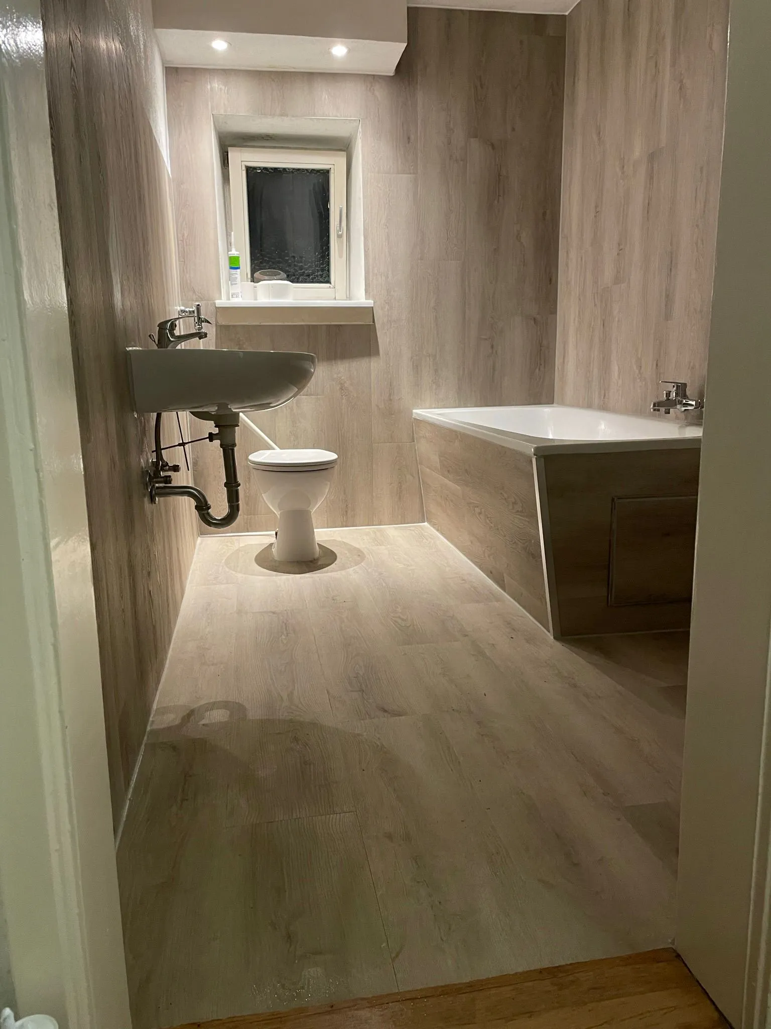 Bad mit greige Holzoptik-Vinyl auf Boden, Wand und Wannenverkleidung