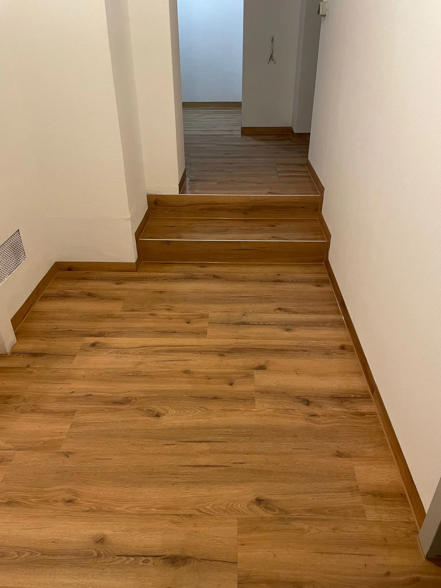 Flur mit goldenen Eichen-Vinyldielen und zwei passend verkleideten Stufen mit Metallprofil